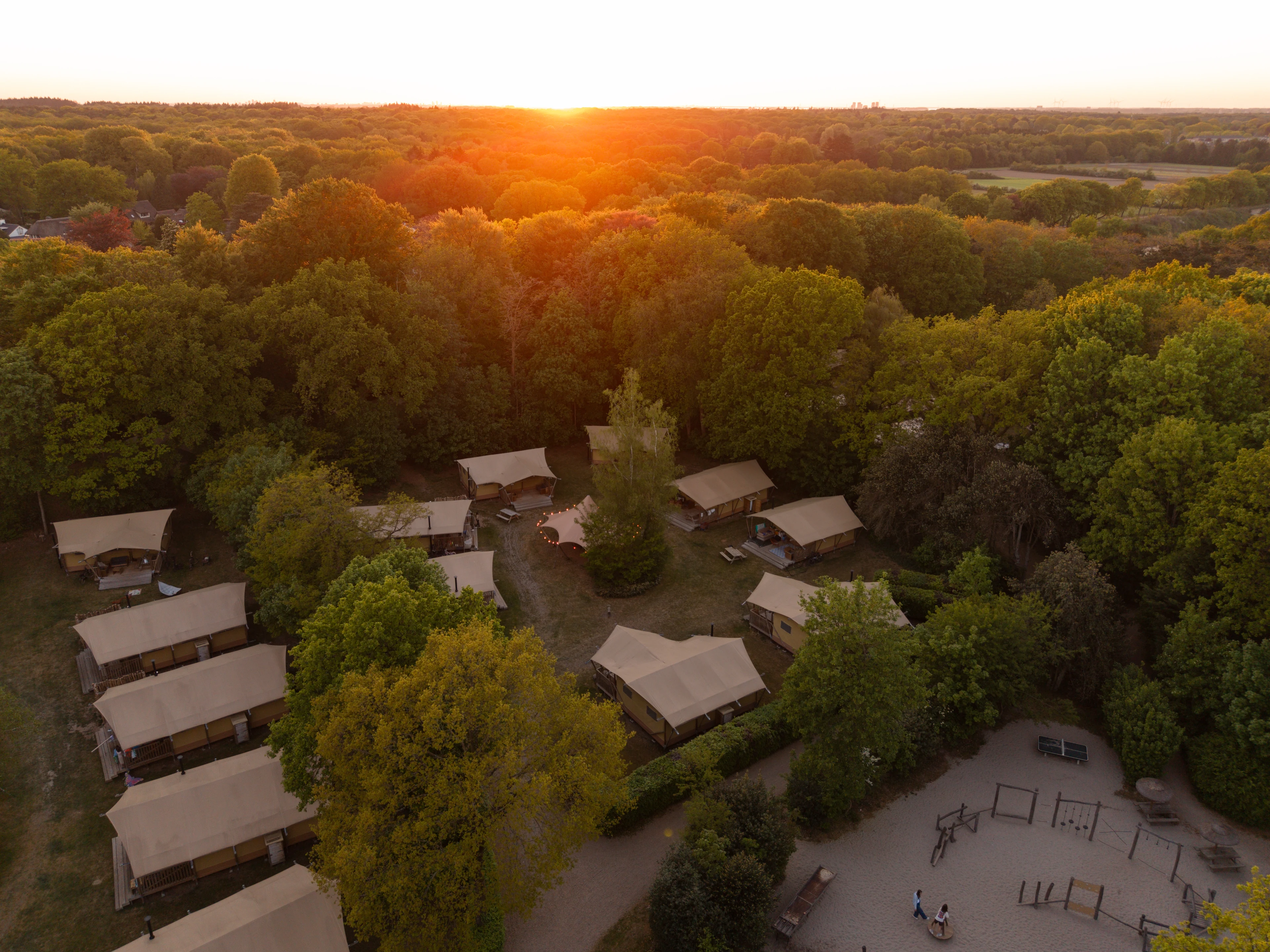 Luchtfoto van een groene camping met glampingtenten bij zonsondergang