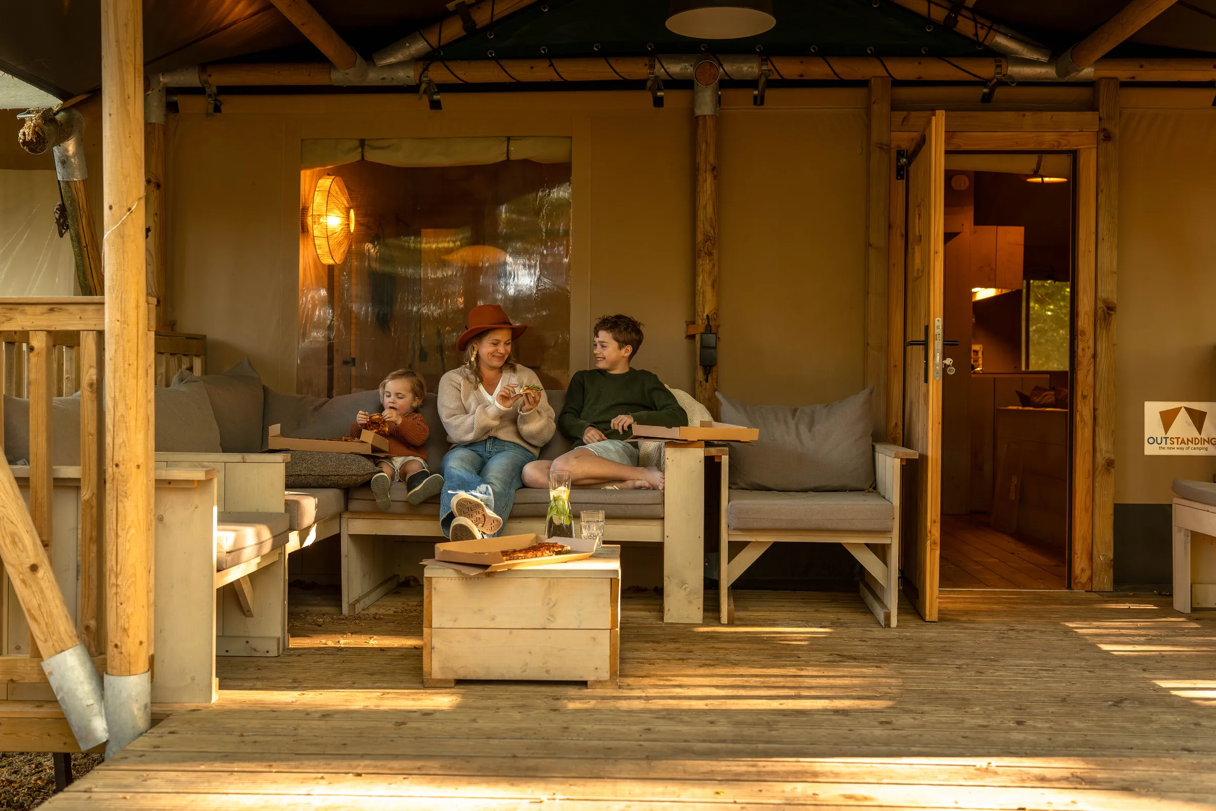 Moeder en twee kinderen eten pizza op de veranda van een safaritent