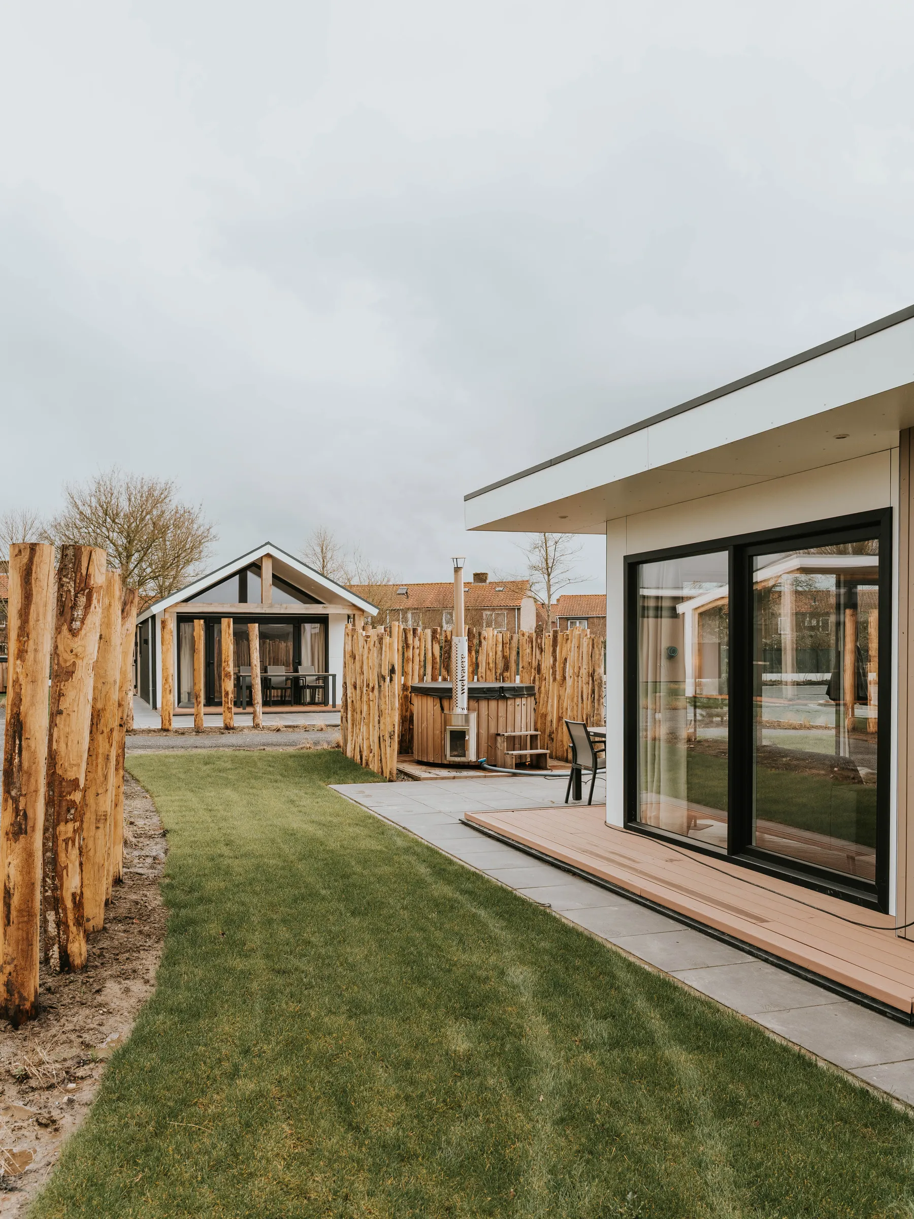 Recreatiewoning met glazen pui en terras aan een gazon, met meer woningen op de achtergrond